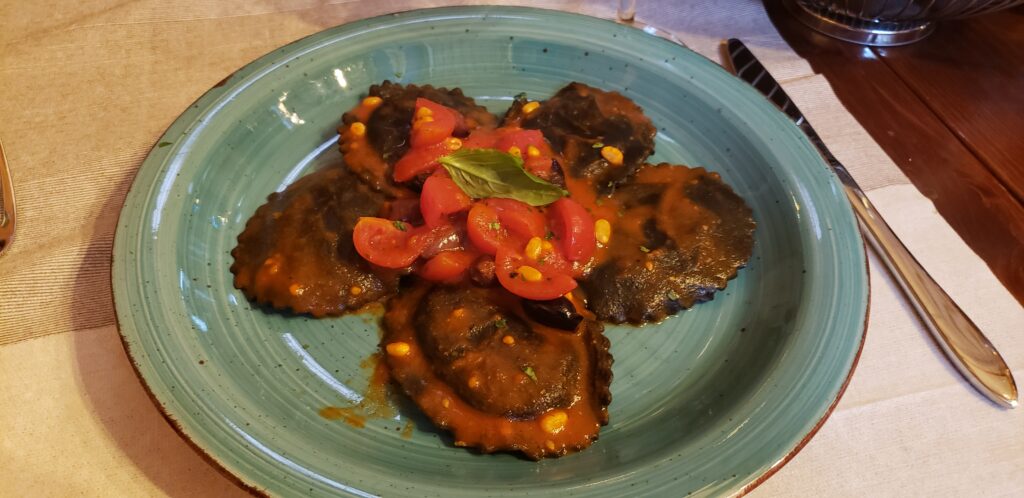 Squid ink pasta, blackish in colour, on a blue plate, served in a restaurant in Venice, Italy.