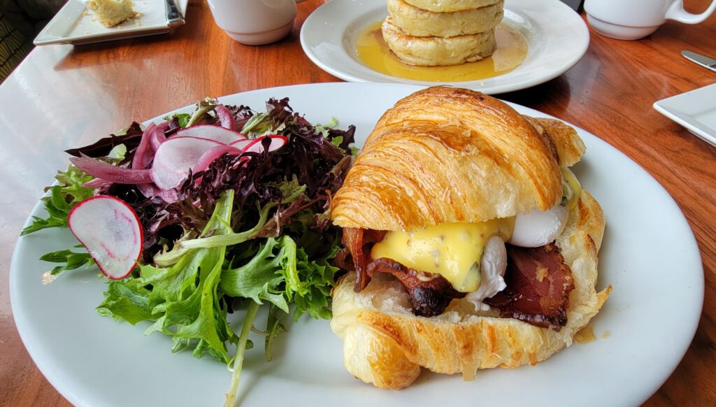 Poached eggs in a croissant with bacon and bearnaise sauce, served with mixed greens on a plate.