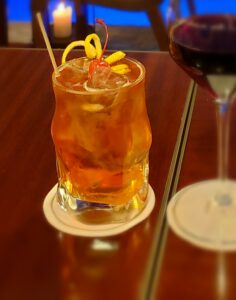 Orange coloured spritz in a glass with zest on top.