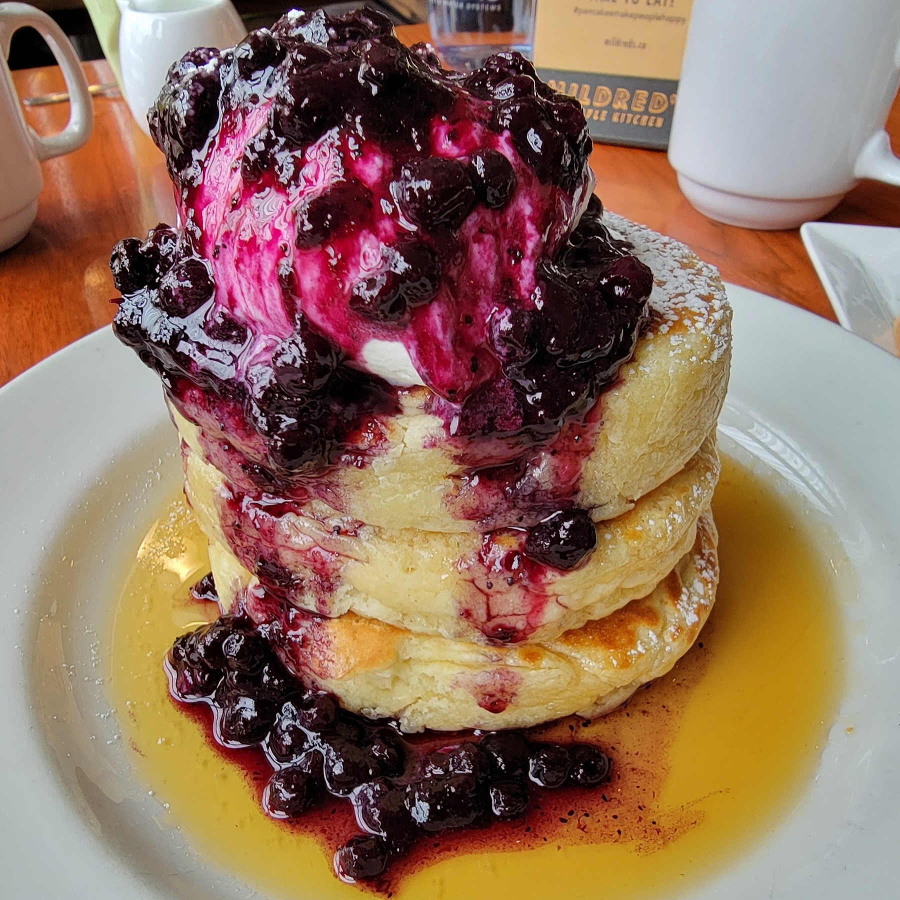 3 pancakes stacked with wild blueberry compote, maple syrup, and whipped cream.