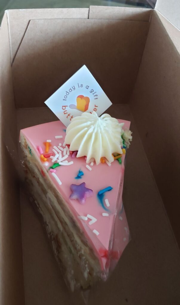 A slice of cake, with colourful sprinkles, in a box.