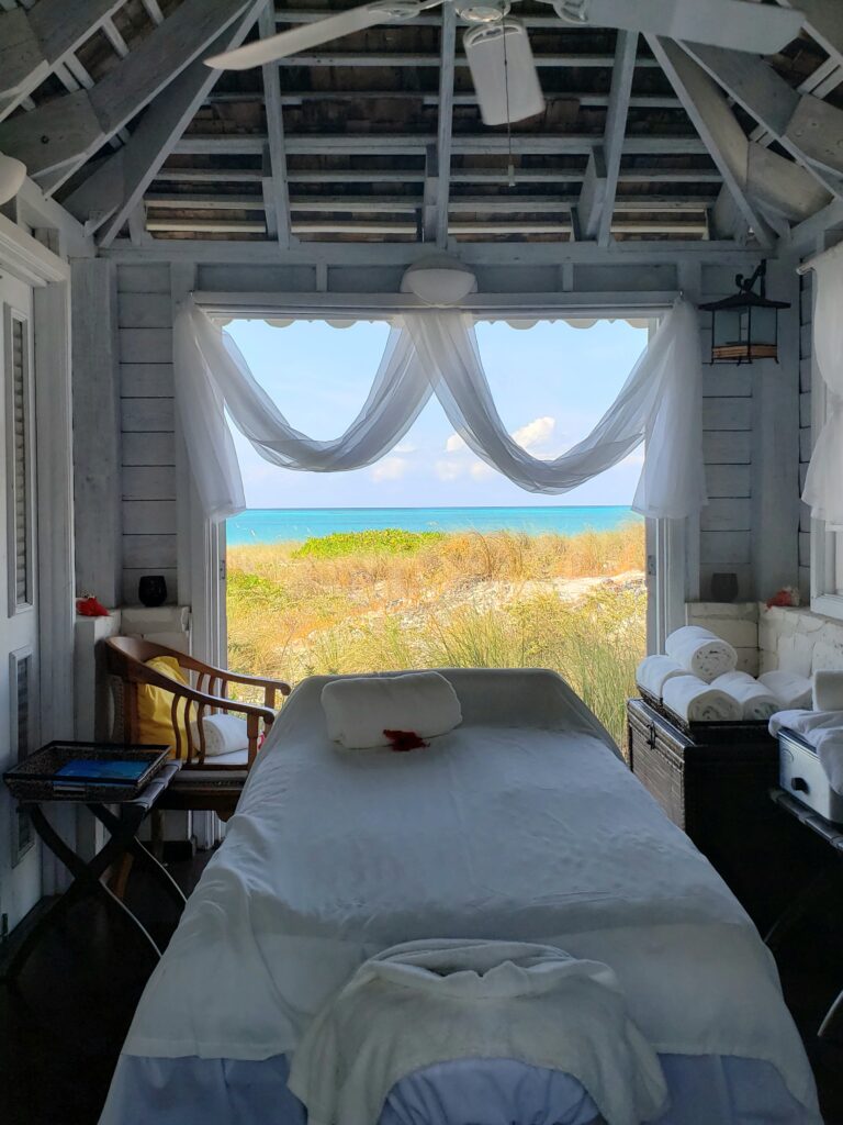 Spa massage table in treatment room with open windows and doors by the beach and ocean at Point Grace