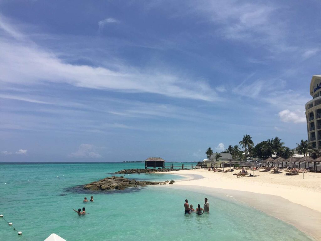 Beach with some guests in the ocean, at Sandals Royal Bahamian.