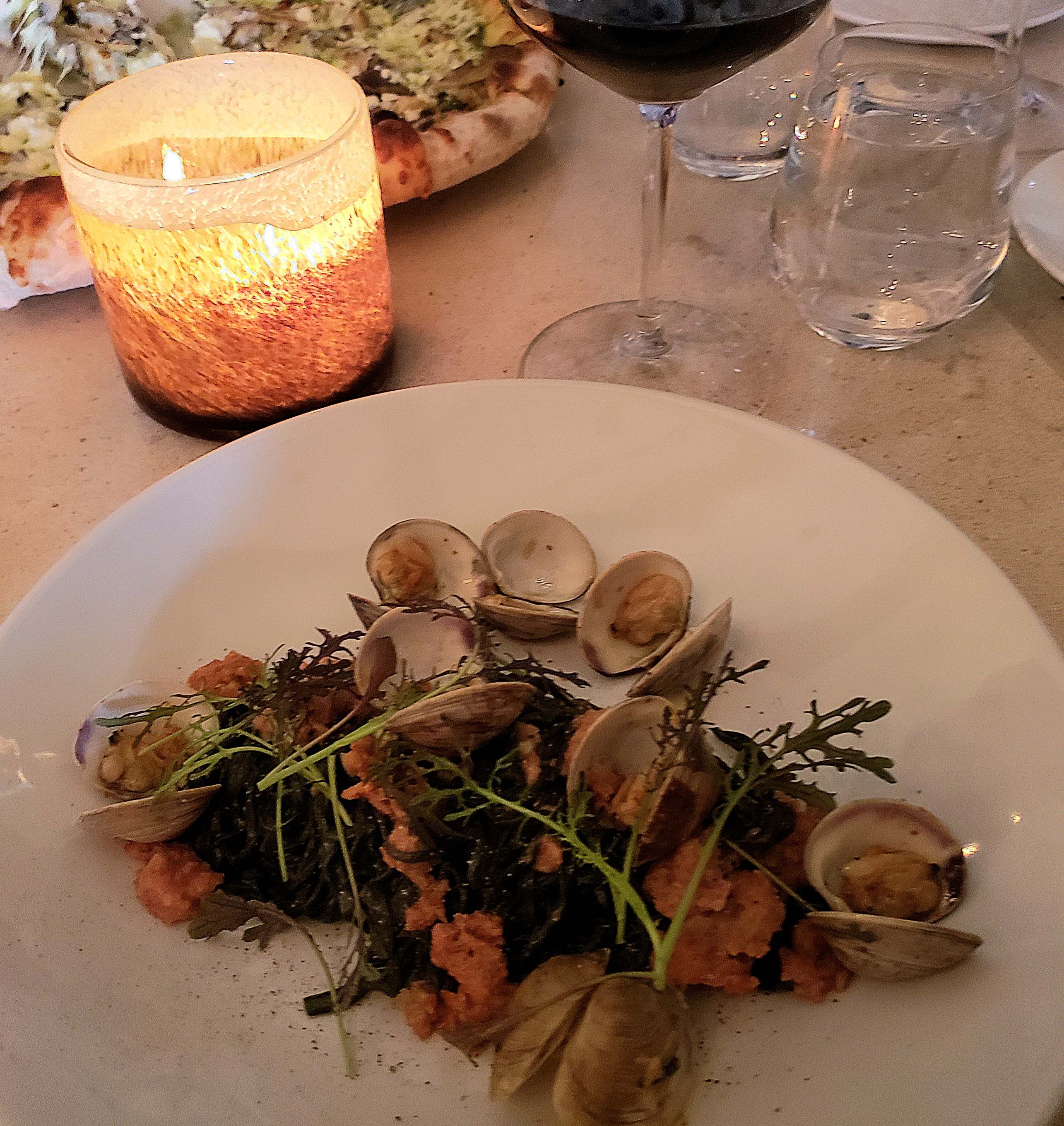 Pasta with clams on white circular plate, with lit candle, glass of wine on table, at Kitchen 76 restaurant in Niagara-on-the-lake.