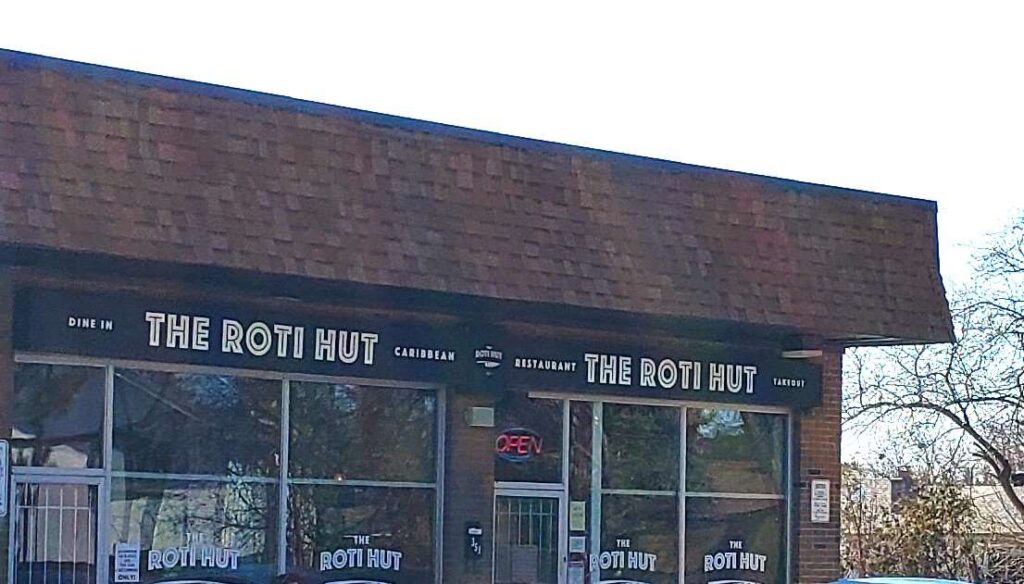 Exterior and sign of The Roti Hut in Scarborough plaza.