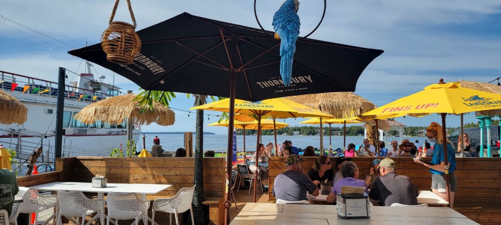 People eating outside on island inspired restaurant patio on a sunny day by the water.