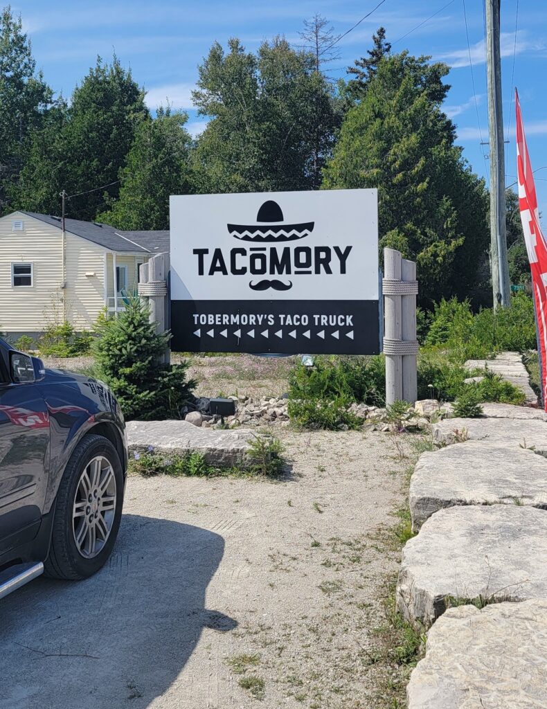 Black and white Tacomory sign by the road for the taco food truck