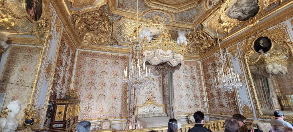 Grand and gold decor in The Queen's Bedchamber with chandelier and mirrors.