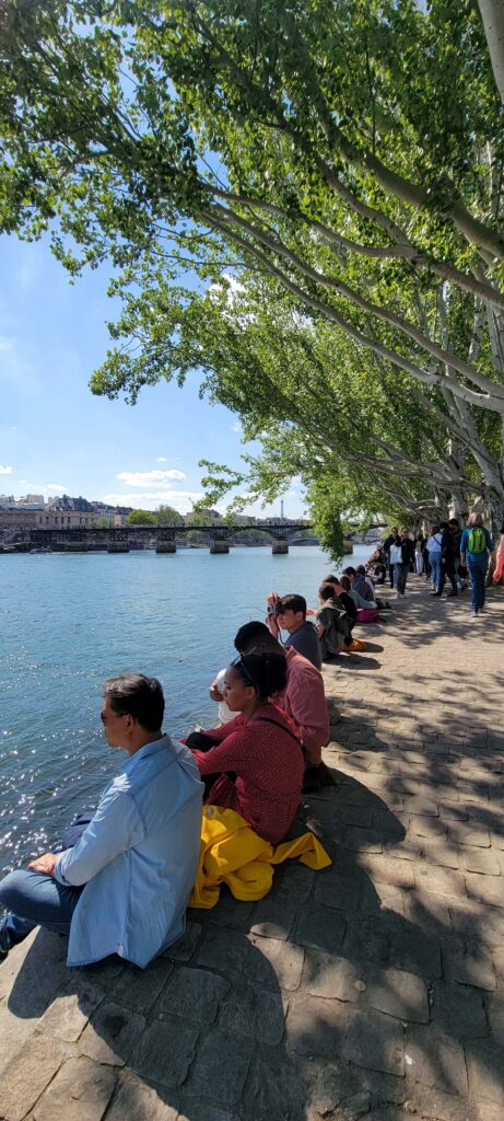 People sitting and walking along the banks of the river Seine in Paris on a sunny day.