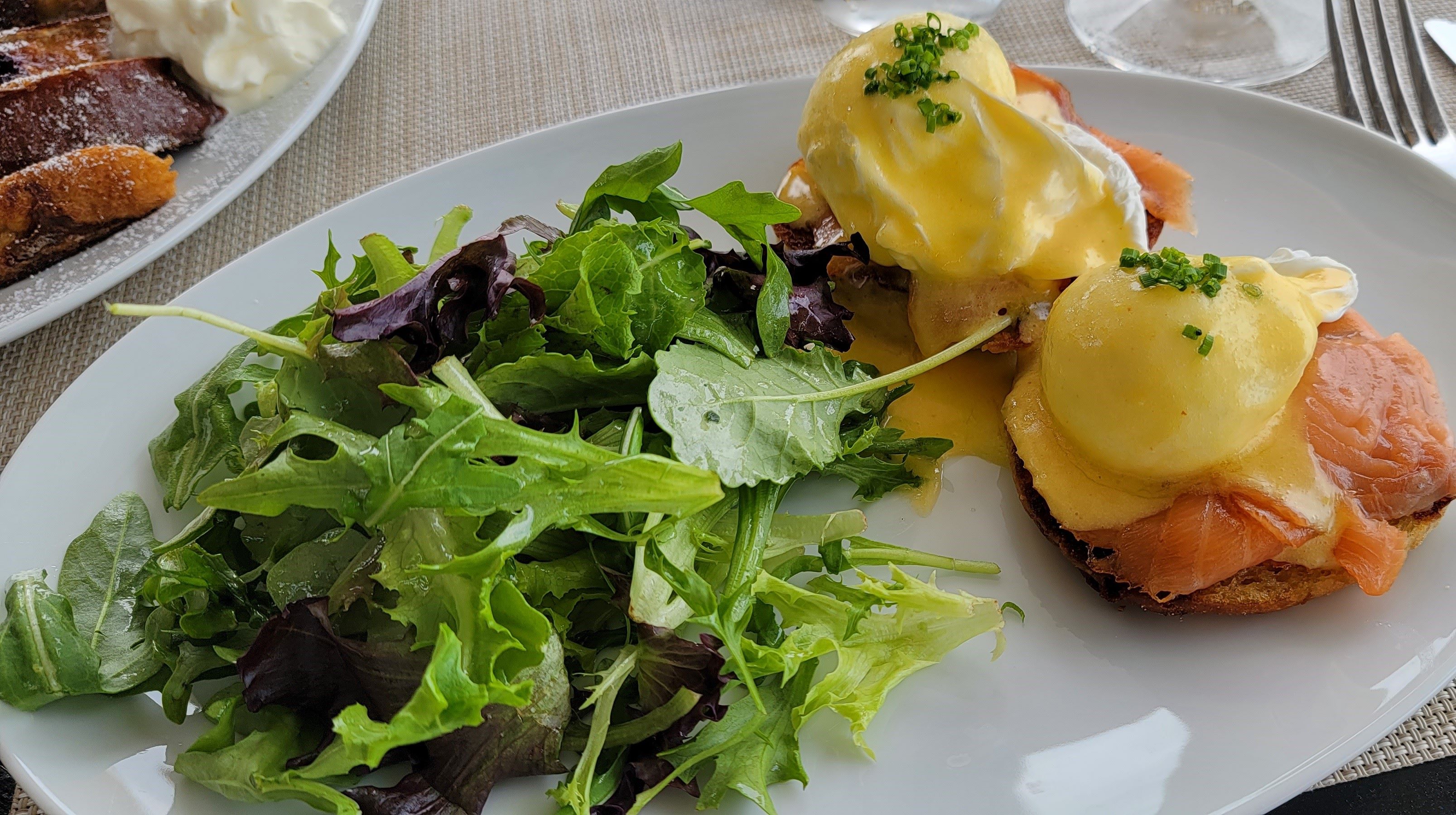 Eggs benedict served with salad on a white plate.