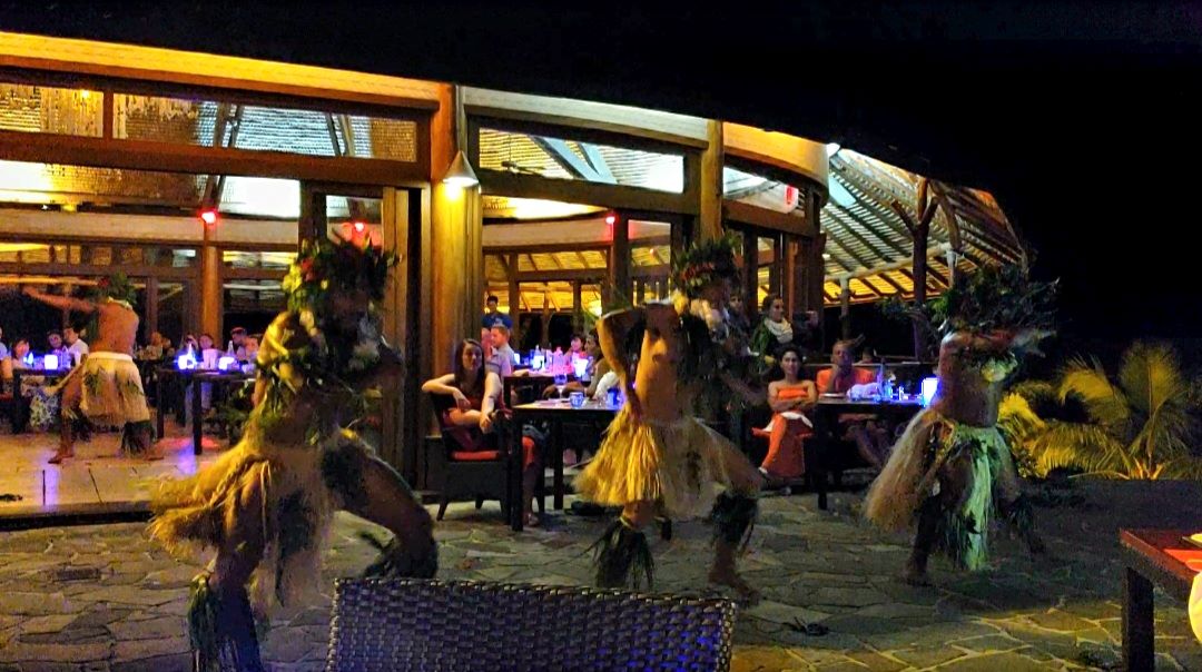 Male dancers in traditional Polynesian dress performing outside.