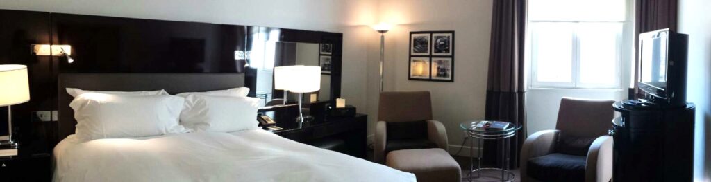 Luxury room in London Sofitel St. James with bed, two chairs, tv and elegant decor.