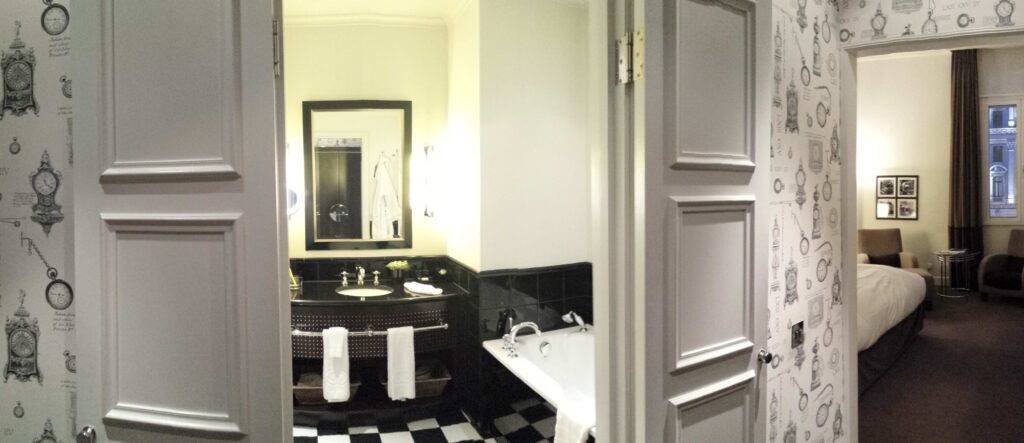 panoramic picture of room which includes bathroom door slightly open and bedroom at the end in Sofitel London St. James.