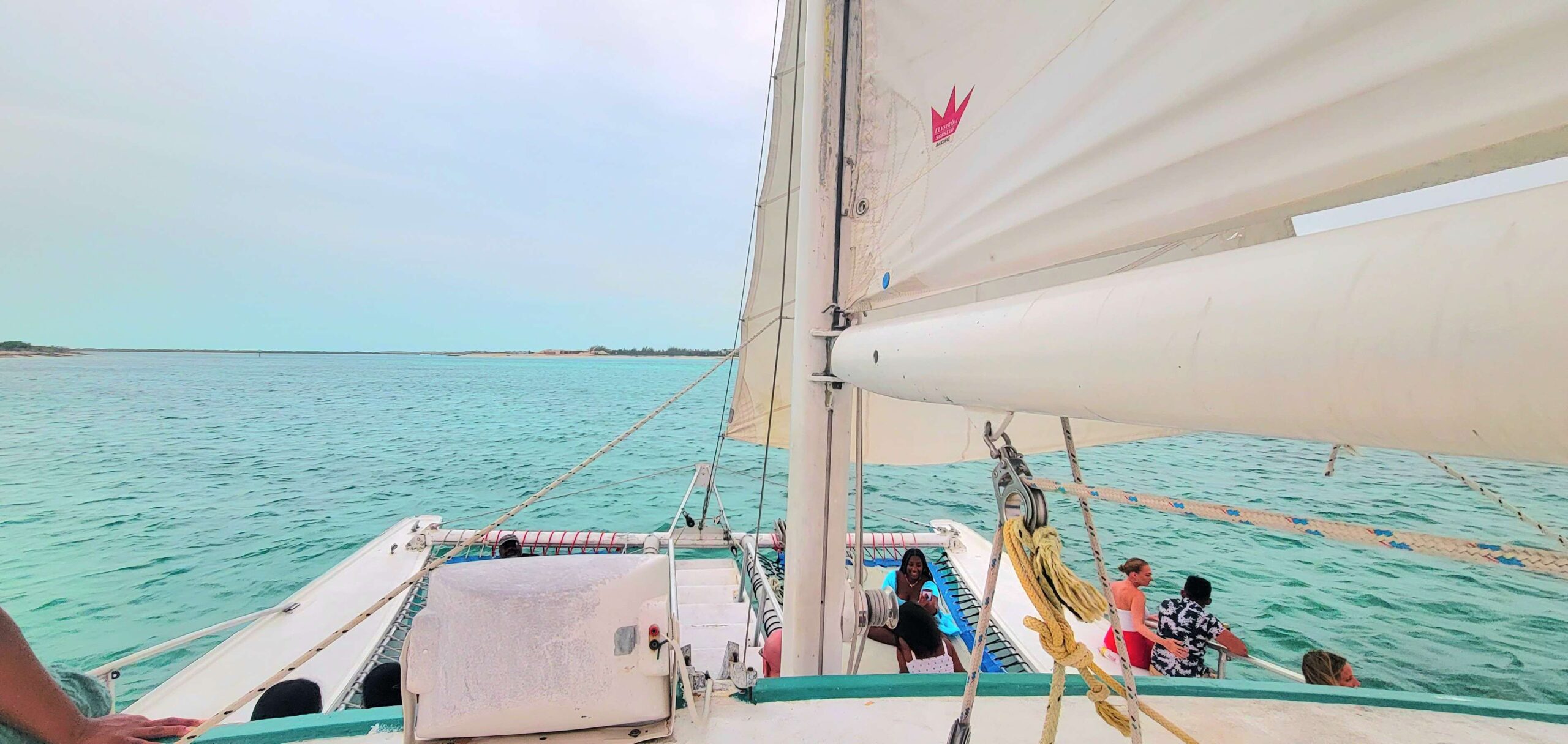 Picture from the top of the catamaran that shows sail and people sitting on the boat.