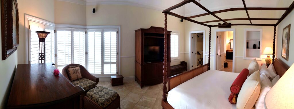 Master bedroom with four poster bed, elegant wooden furniture and windows.