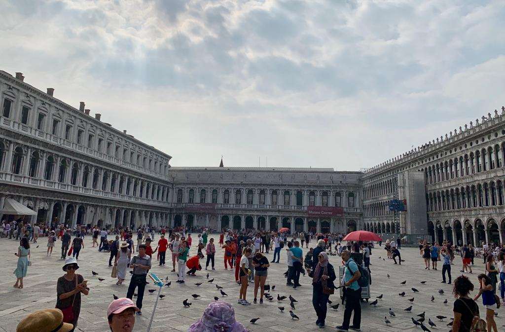 Many visitors and pigeons in Saint Mark's Square during the day in Venice.