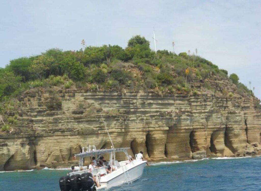 White boat in front of The Pillars of Hercules in Antigua, during snorkel stop during the Xtreme Circumnavigation tour.