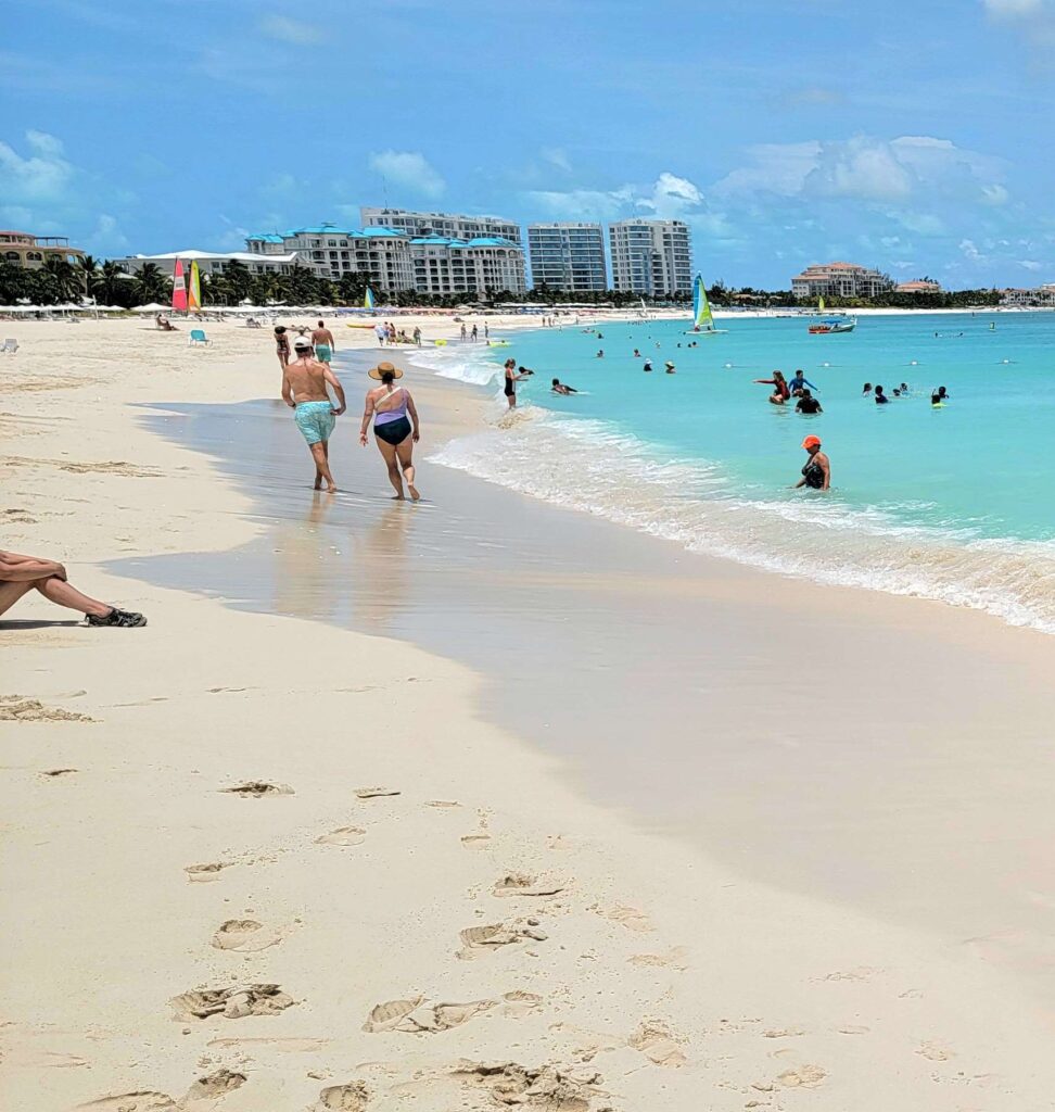 Sunny day on Grace Bay Beach in Turks and Caicos with people walking along the beach and swimming in the ocean.