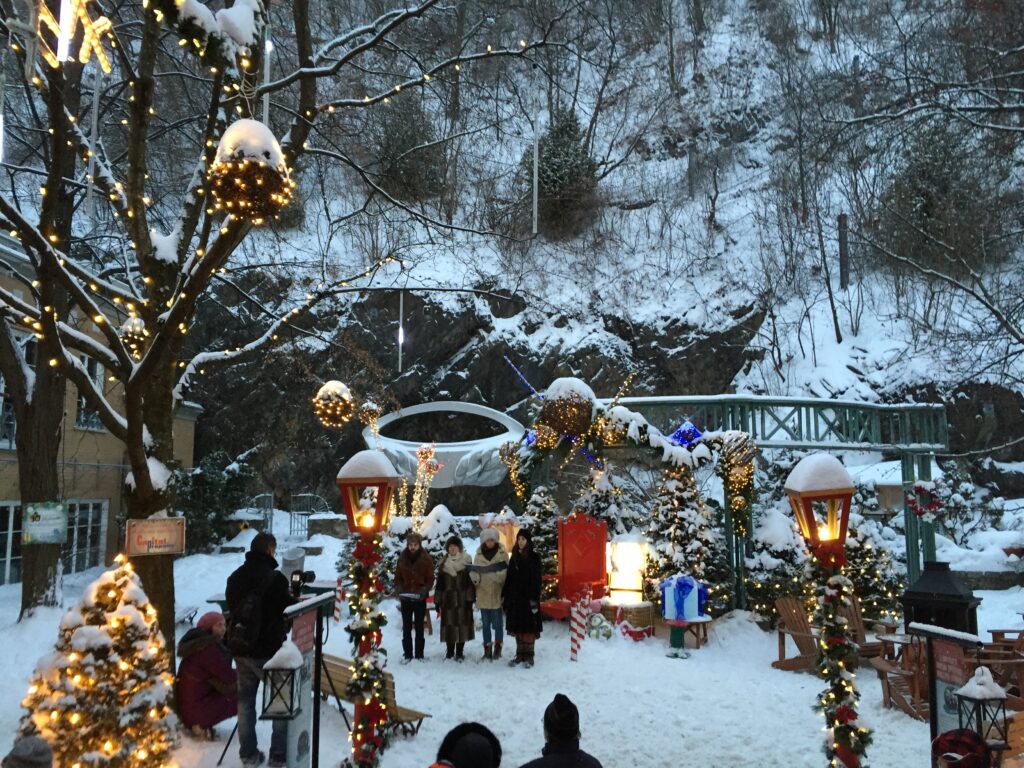 Four people singing carols outside on a snowy winter evening in beautifully decorated spot which was free things to do in Quebec City.