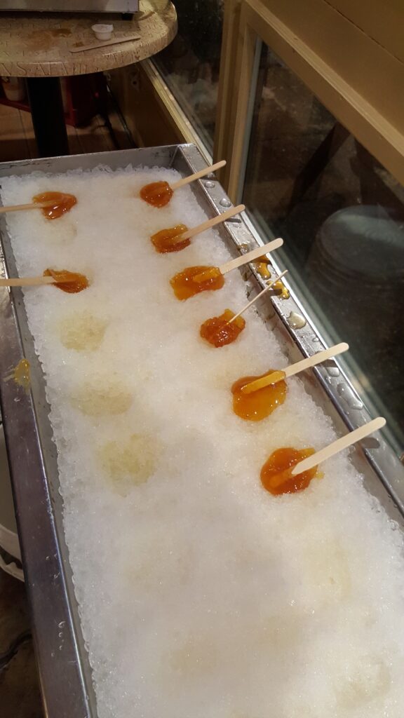 Eight maple syrup taffy treats, on sticks, poured onto snow or crushed ice, in Petit-Champlain in Old Quebec.