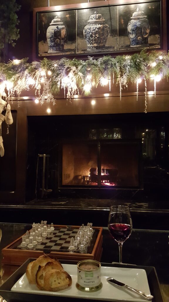 Fireplace in the background of elegant chess set, glass of red wine with duck rillettes and bread at Hotel Le Germain Quebec, from our view on the couch.