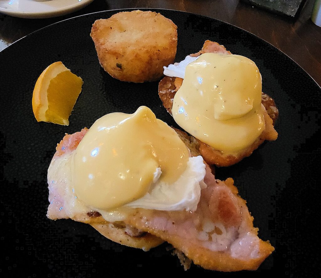 Close up of "Canadian Style Eggs Benedict" served on a black plate, from Zees Grill breakfast menu.