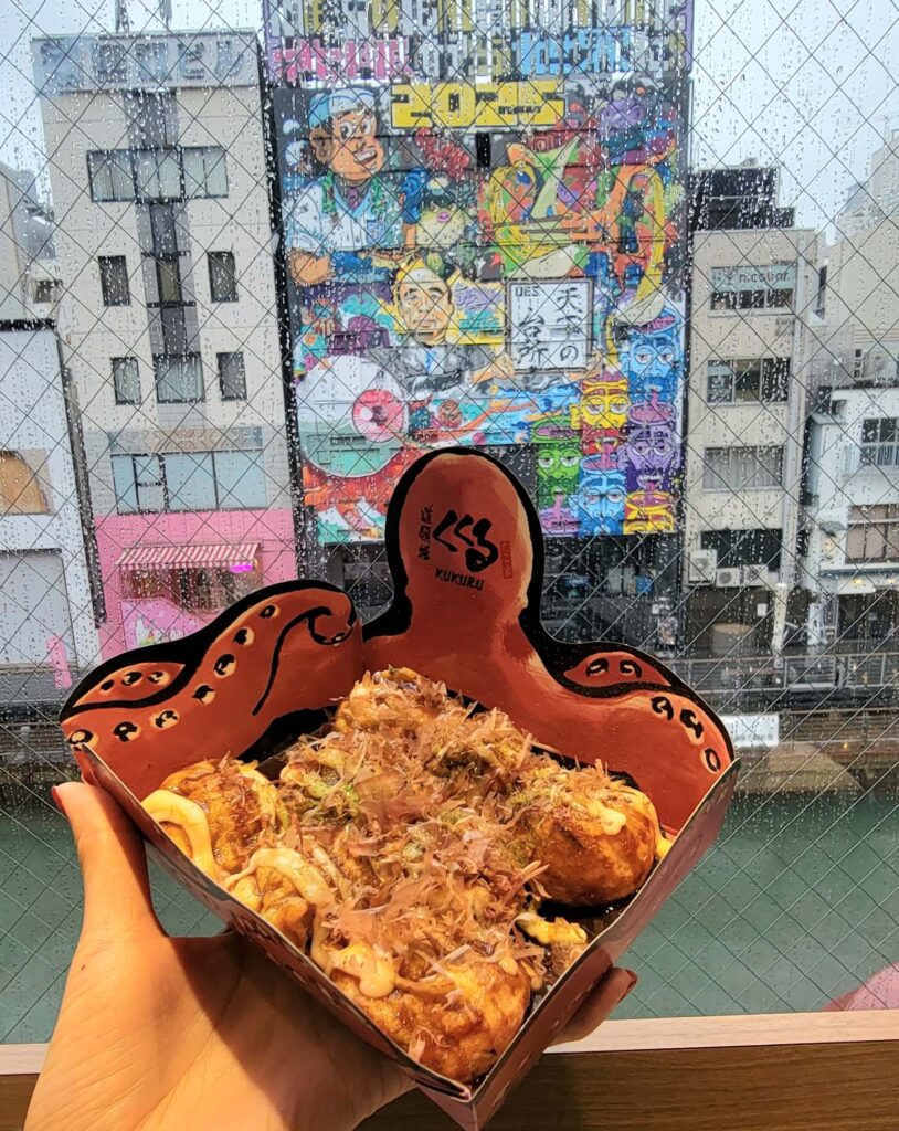 Six takoyaki in square take-out container that looks like an octopus.