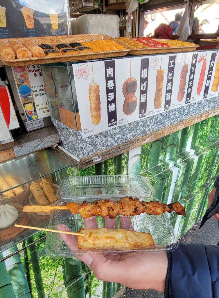 Grilled chicken on a skewer and grilled shrimp fishcake on a skewer in front of food stall.