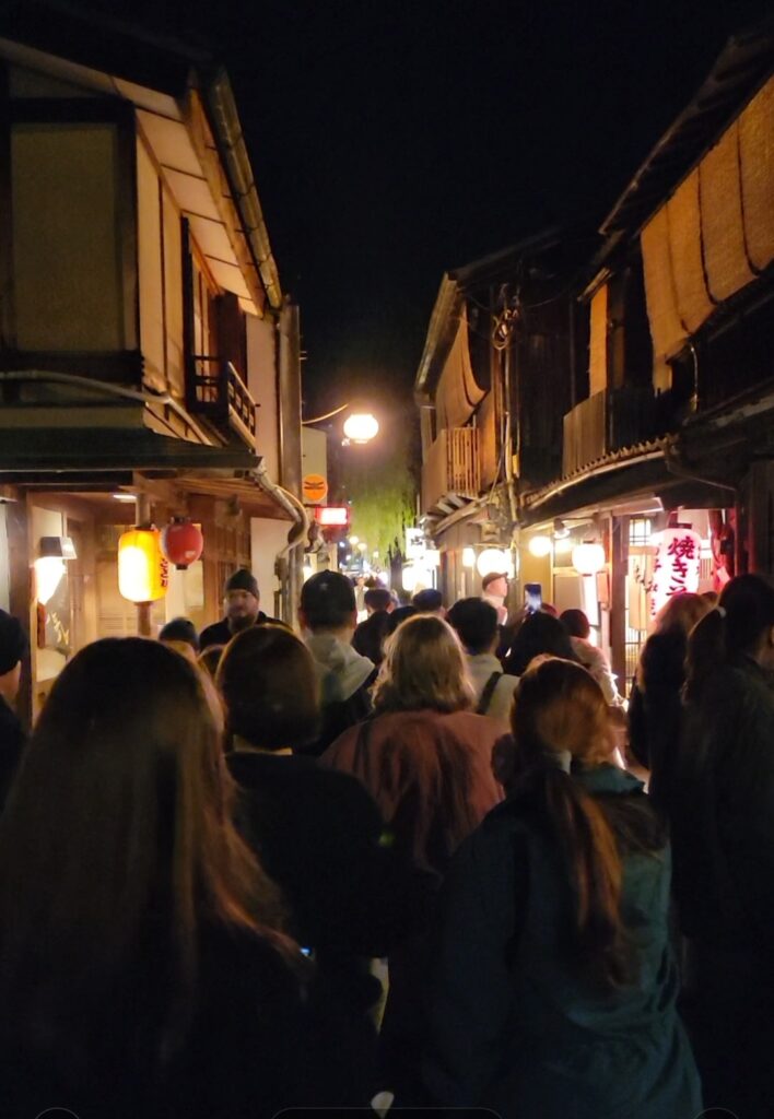 Walking through Pontocho Alley in Kyoto, on a busy and crowded evening, with lit paper laterns in the storefronts.