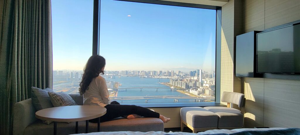 Woman looking at the beautiful Tokyo Bay view during the day, from Superior View room at Mitsui Garden Hotel Toyosu Premier.