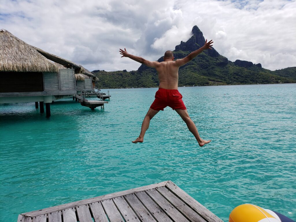 Man in red shorts jumping off the sundeck into the water, Mount Otemanu in the background, at the InterContinental Bora Bora & Thalasso Spa.