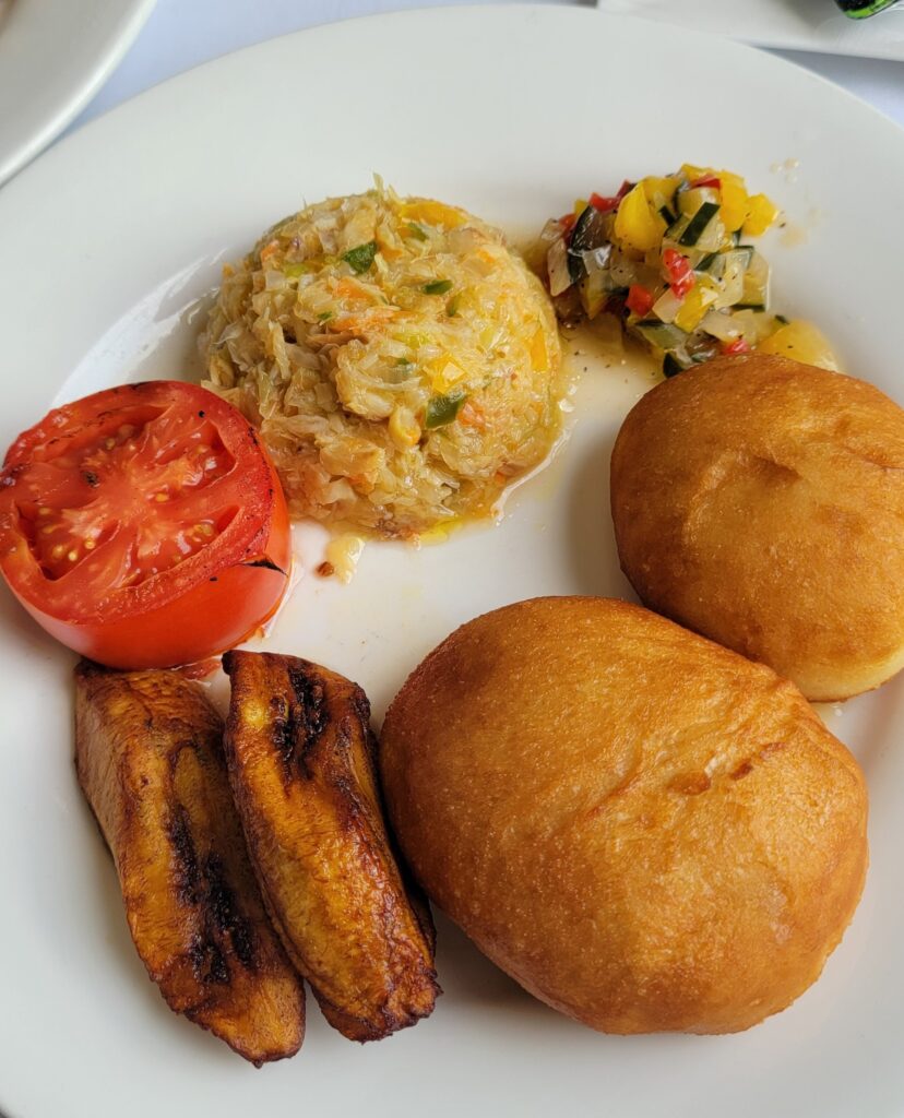 A traditional Grenadian breakfast, must eat foods in Grenada, with bakes, saltfish, fried plantains, roast tomato.