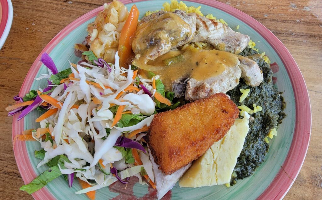 A full plate with grilled fish served with must eat food in Grenada traditional side dishes such as rice and peas, provision, callaloo, macaroni pie. 