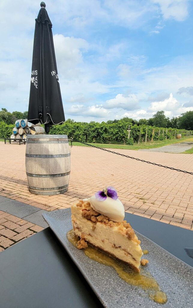 Slice of peach cobbler cheesecake with purple flower on top of ice cream, from Inniskillin Winery Niagara Estate Grill, one of our favourite Niagara-on-the-Lake restaurants with a beautiful view of vineyards, on a sunny day.