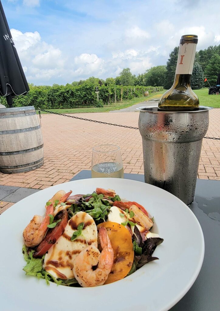 Caprese salad with grilled shrimp and wine from Inniskillin Winery Niagara Estate Grill, one of our favourite Niagara-on-the-Lake restaurants with a beautiful view of vineyards, on a sunny day.